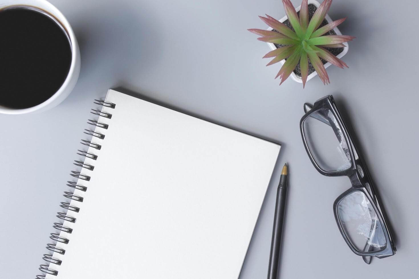 A flat lay of a journal, coffee, and reading glasses